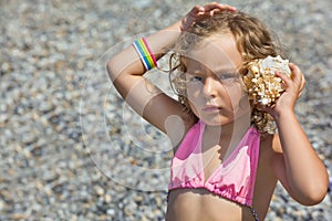 Little girl has leant seashell bowl to an ear