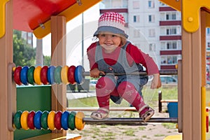 Little girl in hat climbs on children playground at sunny