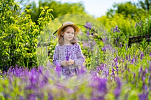 Little girl in hat picking a bouquet of wildflowers in a meadow