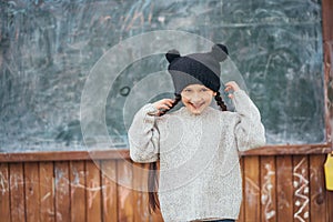 Little girl in a hat posing on the background of the school blackboard