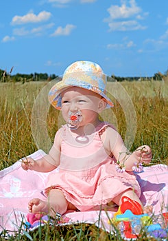 Little girl in a hat sitting on green field