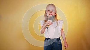 Little girl in hat and sunglasses singing into a microphone and dancing happily.