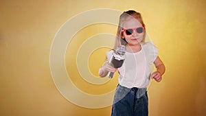 Little girl in hat and sunglasses singing into a microphone and dancing happily.