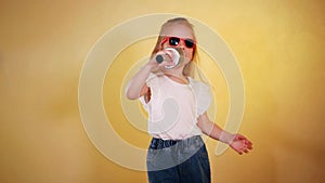 Little girl in hat and sunglasses singing into a microphone and dancing happily.