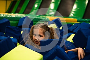 Little girl having fun in a dry pool with bright soft cubes to jump into. Kids playing room