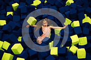 Little girl having fun in a dry pool with bright soft cubes to jump into. Kids playing room