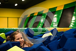 Little girl having fun in a dry pool with bright soft cubes to jump into. Kids playing room