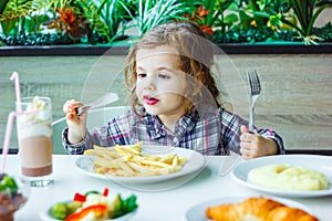 Little girl having lunch in the restaurant with the table knife and fork in hands.