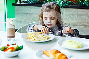 Little girl having lunch in the restaurant with the table knife and fork in hands.