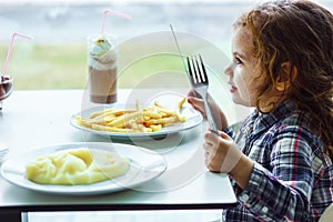 Little girl having lunch in the restaurant with the table knife and fork in hands.