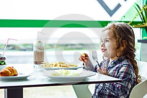 Little girl having lunch in the restaurant with the table knife and fork in hands.