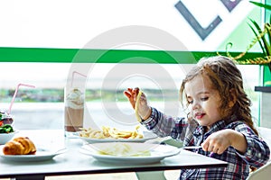 Little girl having lunch in the restaurant with the table knife and fork in hands.