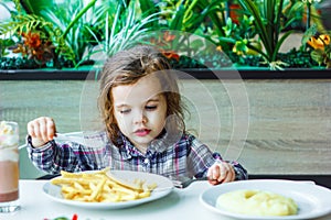 Little girl having lunch in the restaurant with the table knife and fork in hands.