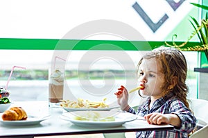 Little girl having lunch in the restaurant with the table knife and fork in hands.