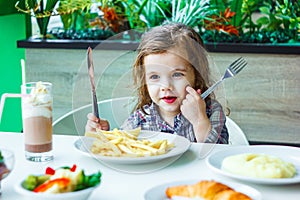 Little girl having lunch in the restaurant with the table knife and fork in hands.