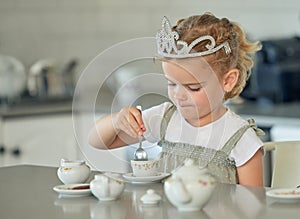 A little girl having a tea party at home. Cute brunette female wearing a tiara while playing with tea set and having