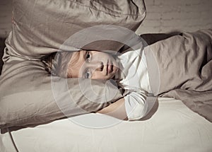 Little girl having trouble sleeping at night holding pillow covering her head and ears upset