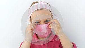 Little girl in headband and protective pink mask against coronavirus COVID-19 pandemic white background on quarantine