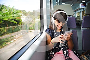 Little girl with headphones and smart phone travelling by train