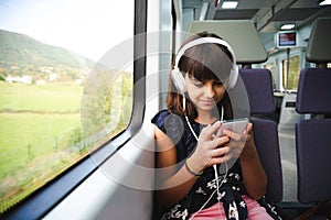 Little girl with headphones and smart phone travelling by train