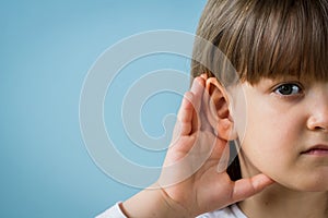 Little girl with hearing problem on light blue background. Close up, copy space