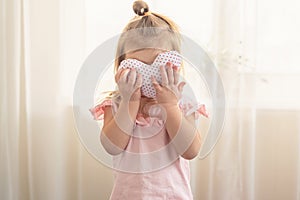 Little girl with heart shaped pillow indoor, hiding behind heart. Concept of love, happiness, kindness, gift, handmade