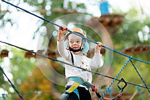 Little girl in helmet climbs ropes in adventure park outdoors. Extreme sport, active leisure on nature