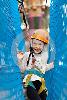 Little girl in helmet climbs ropes in adventure park outdoors. Extreme sport, active leisure on nature