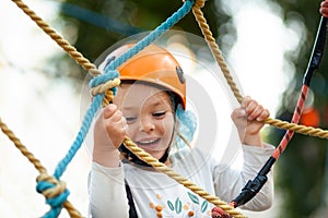 Little girl in helmet climbs ropes in adventure park outdoors. Extreme sport, active leisure on nature