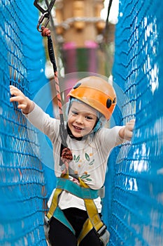 Little girl in helmet climbs ropes in adventure park outdoors. Extreme sport, active leisure on nature