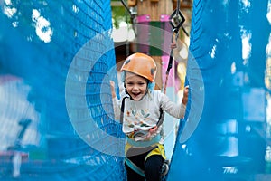 Little girl in helmet climbs ropes in adventure park outdoors. Extreme sport, active leisure on nature