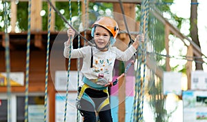 Little girl in helmet climbs ropes in adventure park outdoors. Extreme sport, active leisure on nature