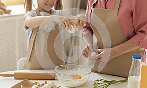 Little girl helping her granny to bake, adding egg to flour in kitchen, close up