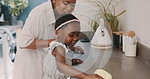 Little girl helping her mother with household chores at home. Happy mom and daughter wearing gloves while spraying and