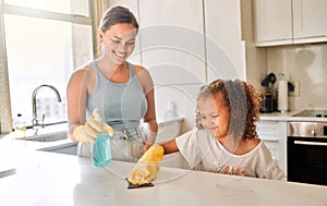 Little girl helping her mother with household chores at home. Happy mom and daughter wearing gloves while spraying and