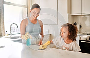 Little girl helping her mother with household chores at home. Happy mom and daughter wearing gloves while spraying and