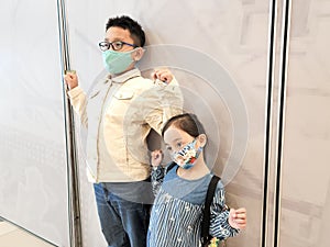 A little girl and her big brother are wearing face masks while standing in public.