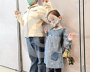 A little girl and her big brother are wearing face masks while standing in public.