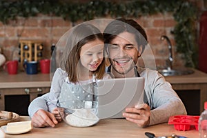 Little girl and her dad using digital tablet in kitchen, checking recipe