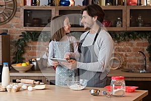 Little girl and her dad using digital tablet at kitchen, checking recipe