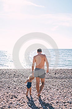Little girl with her dad walks along the beach to the sea. Back view