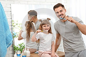 Little girl and her father brushing teeth together in bathroom