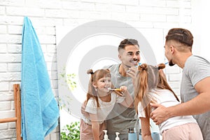 Little girl and her father brushing teeth together near mirror in bathroom at home.