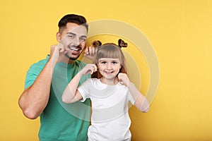 Little girl and her father flossing teeth on color background photo