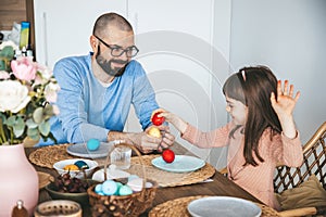Little girl and her father playing an egg fight game with red Easter eggs. Celebrating and eating Easter breakfast concept