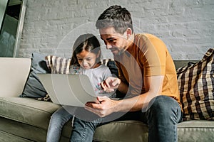 Little girl and her father using a laptop together at home.