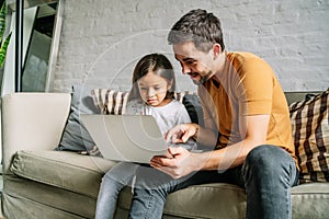 Little girl and her father using a laptop together at home.