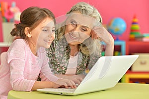 little girl with her grandmother playing computer game with laptop