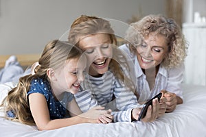 Little girl her mom and granny using smartphone on bed