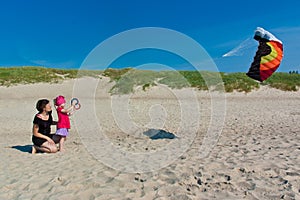 Little girl with her mom playing a kite on the beach